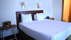 A neatly made bed with white linens, a small bedside table with a radio, and two wall-mounted lamps. - #14 ONE KING BED in delightful Columbia Falls with WiFi, AC 20 miles from GNP (Columbia Falls)