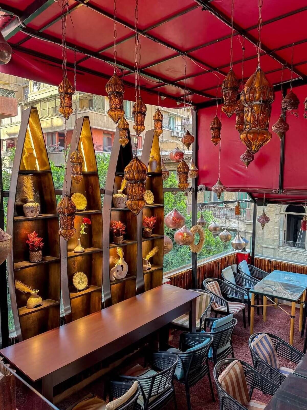 An outdoor seating area with tables and chairs, decorative hanging lamps, and shelves with various items.