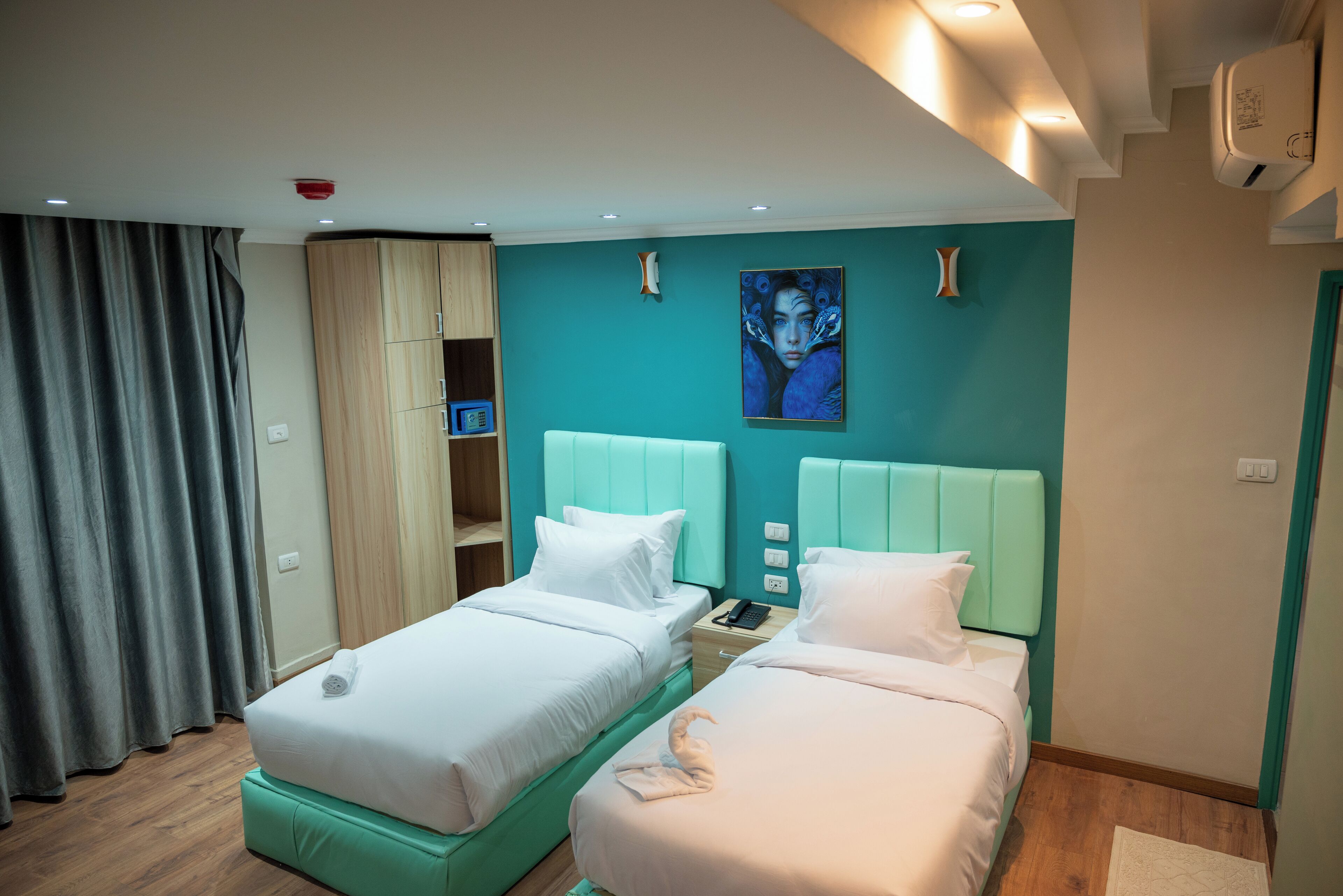 Une chambre d’hôtel avec deux lits simples, une armoire, un bureau et un tableau au mur.