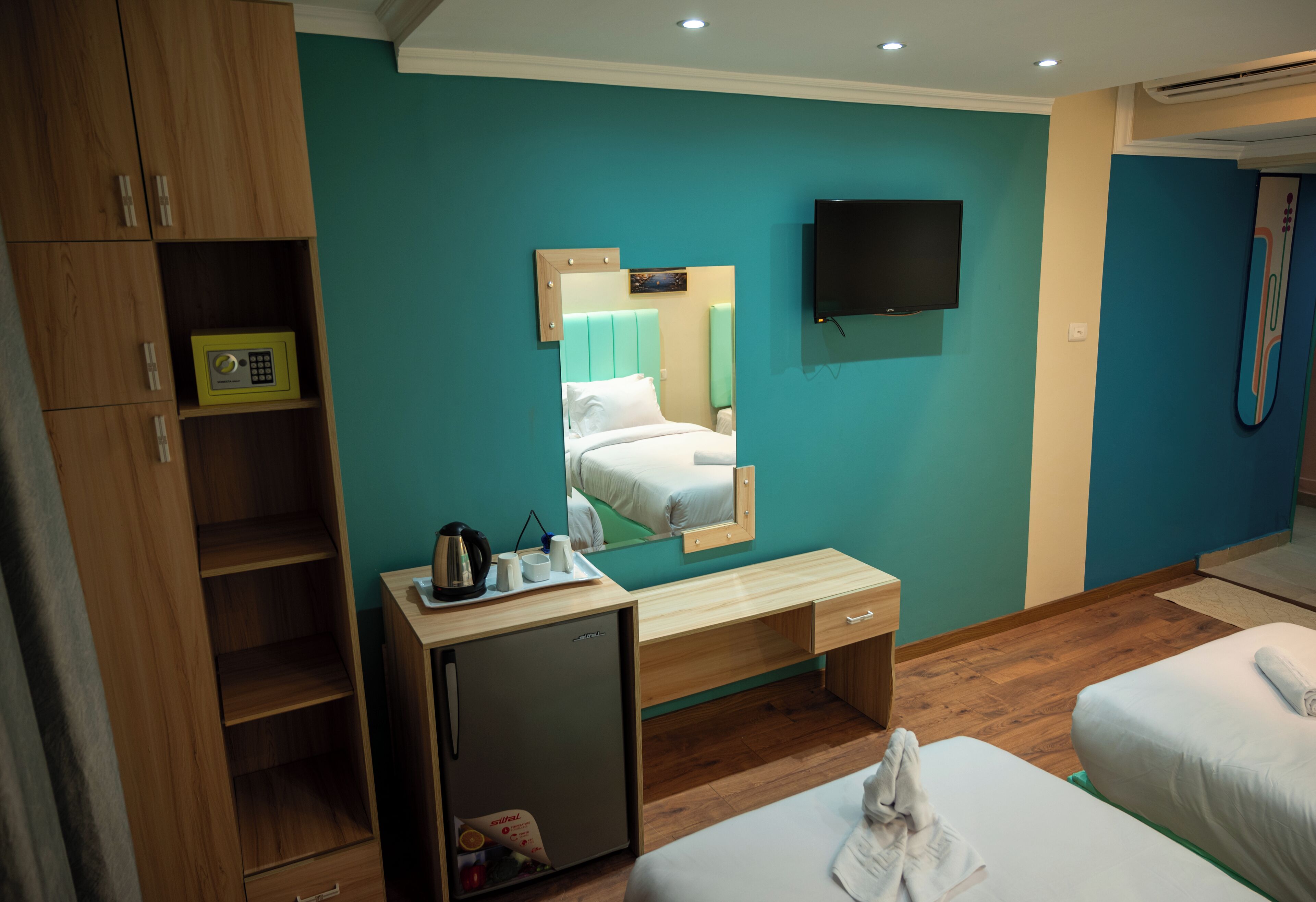 Hotellihuone, jossa on sänky, työpöytä, pieni jääkaappi, televisio ja kylpyhuone, jossa on suihku.