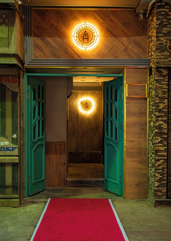 A hotel entrance with a red carpet, wooden flooring, and a circular illuminated sign above the door. - Soft Hotel (Cairo)