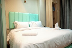 Una cama bien hecha con sábanas blancas y un cabecero color aguamarina, un armario de madera y una toalla doblada sobre la cama.