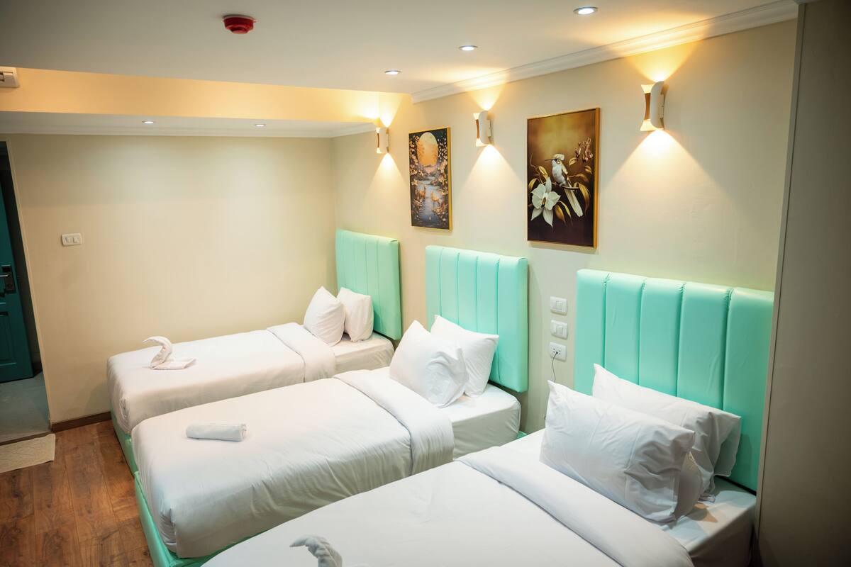 A hotel room with two beds, each with white bedding and pillows, and teal headboards.