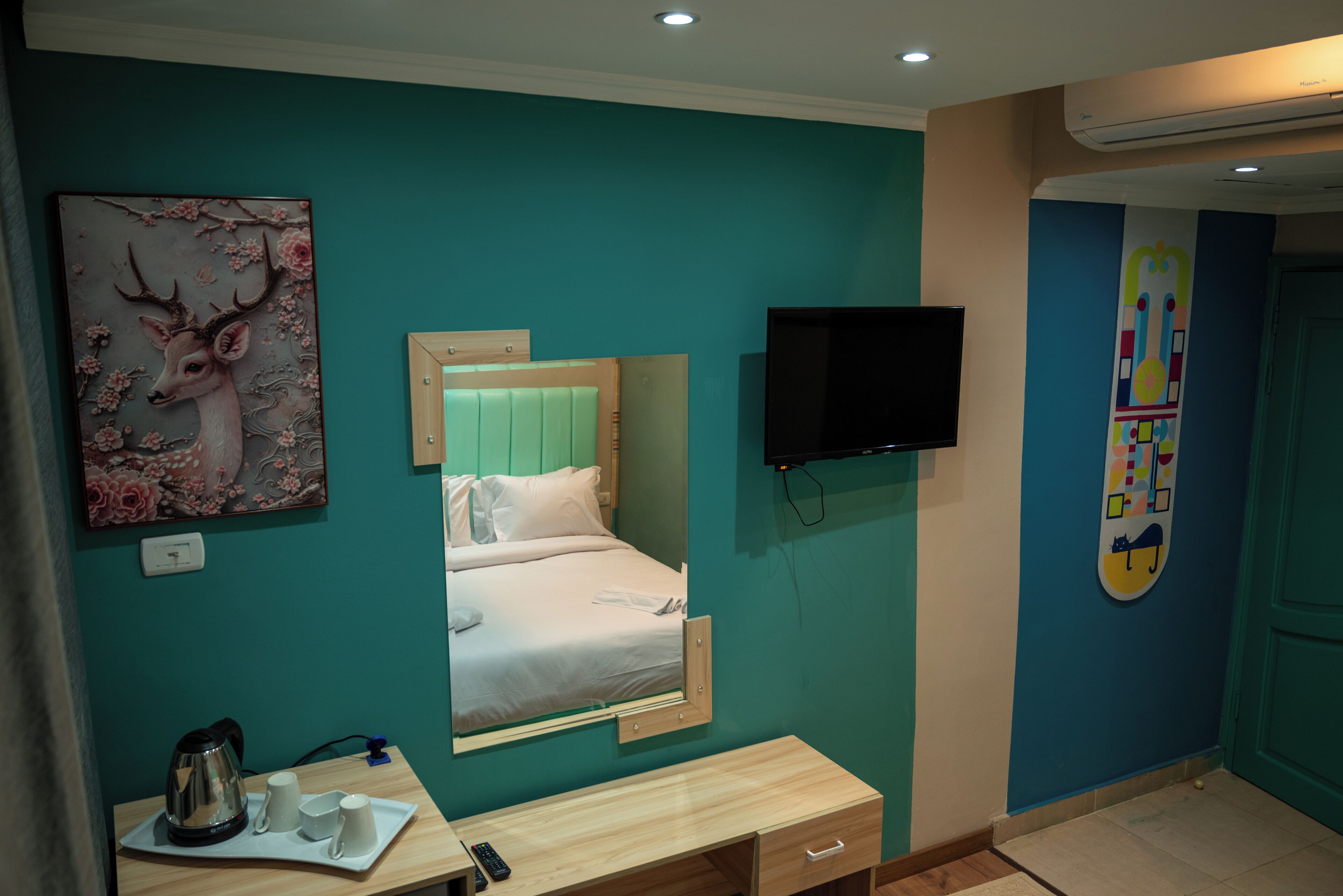 Habitación de hotel con una cama, un escritorio con hervidor y tazas, un televisor y un cuadro de un ciervo.