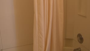 A bathtub with a shower curtain, a handheld showerhead, and a small shelf. - #15 ONE QUEEN BED with WiFi and AC in charming Columbia Falls, 20 mi from GNP!! (Columbia Falls)