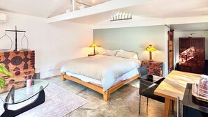 Un dormitorio moderno con una cama, lámparas de noche, una mesita de cristal y un escritorio de madera.