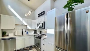 Una cocina moderna con armarios blancos, electrodomésticos de acero inoxidable y un refrigerador grande.