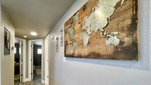 A hallway with a large, textured map on the wall, wooden flooring, and a door leading to another room.
