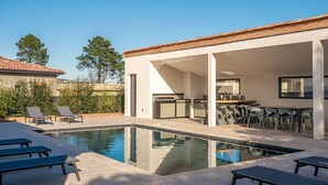 A modern outdoor pool area with lounge chairs, a bar, and a covered seating area.