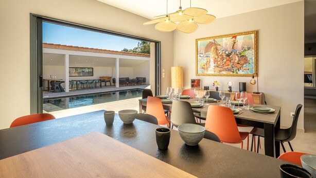 A dining area with a pool view, modern furniture, and a large painting.