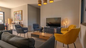 A modern living room with a flat-screen TV, two sofas, a coffee table, and a bookshelf.