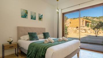 A bedroom with a large bed, a nightstand, and a view of a stone building outside.