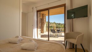 Una camera d'albergo con un letto, una televisione, una sedia e vista su un patio esterno con tavolo e sedie.