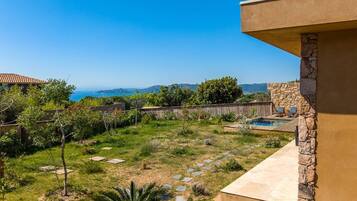 A backyard with a stone wall, a swimming pool, and a view of the ocean.