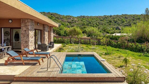 Zona piscina con sedie a sdraio, piscina e vista su una collina.