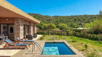 A poolside area with lounge chairs, a pool, and a view of a hillside.