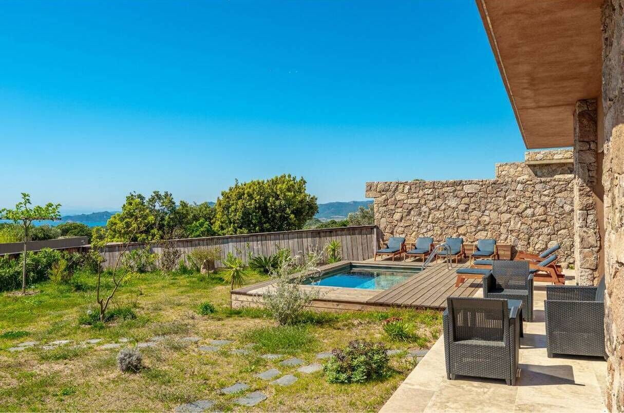 Un patio trasero con piscina, mobiliario exterior y un muro de piedra.