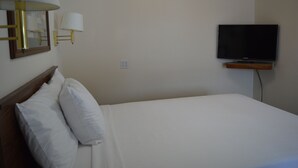 A hotel room with a bed, white pillows, a flat-screen TV mounted on the wall, and a bedside table. - #16 FAMILY SUITE , 3 BEDS with WiFi, and AC in Columbia Falls, 20 mi to GNP (Columbia Falls)