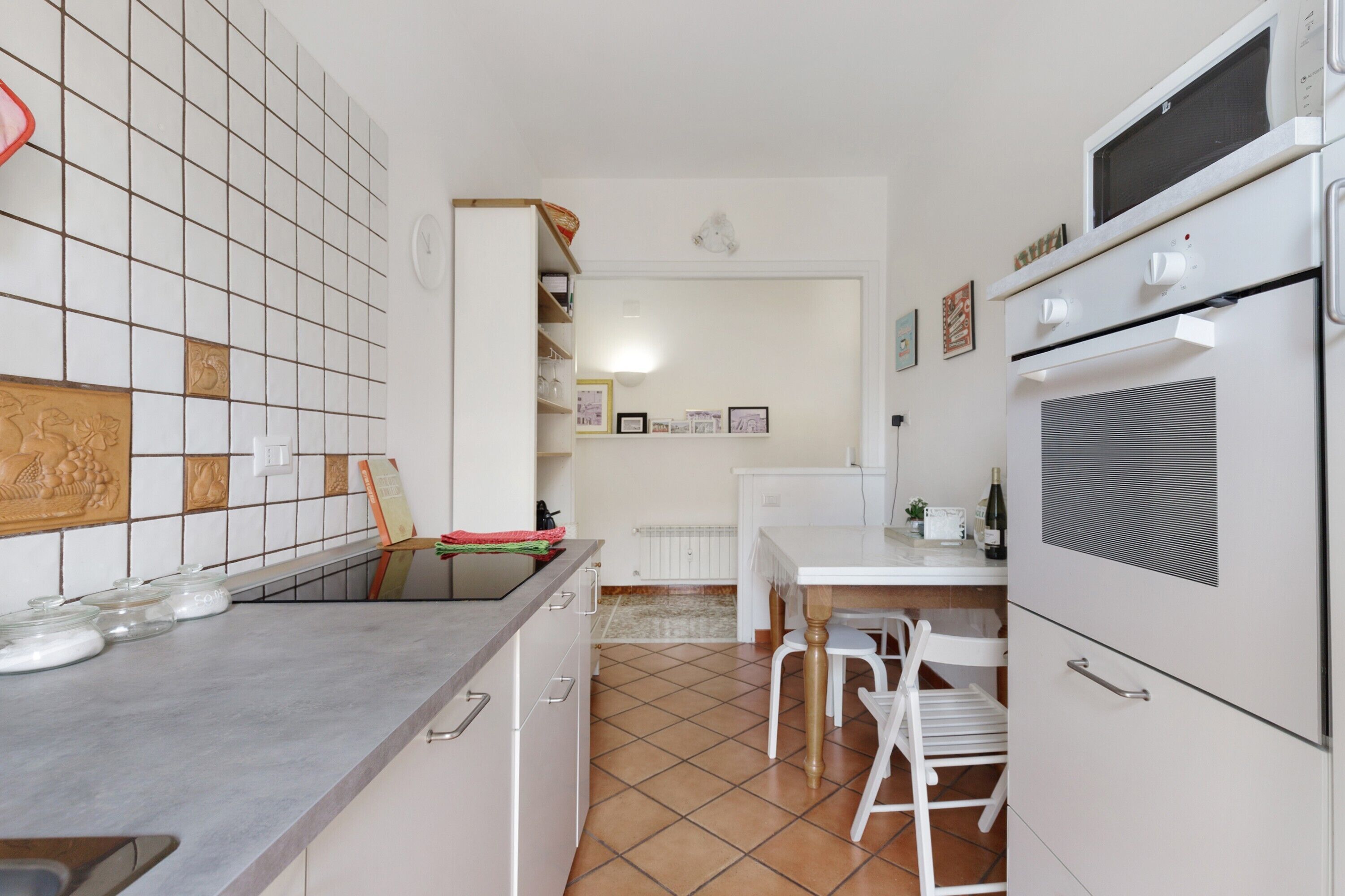 Une cuisine avec un mur recouvert de carreaux, un plan de travail orné de bocaux en verre, une table à manger avec des chaises et un four encastré.