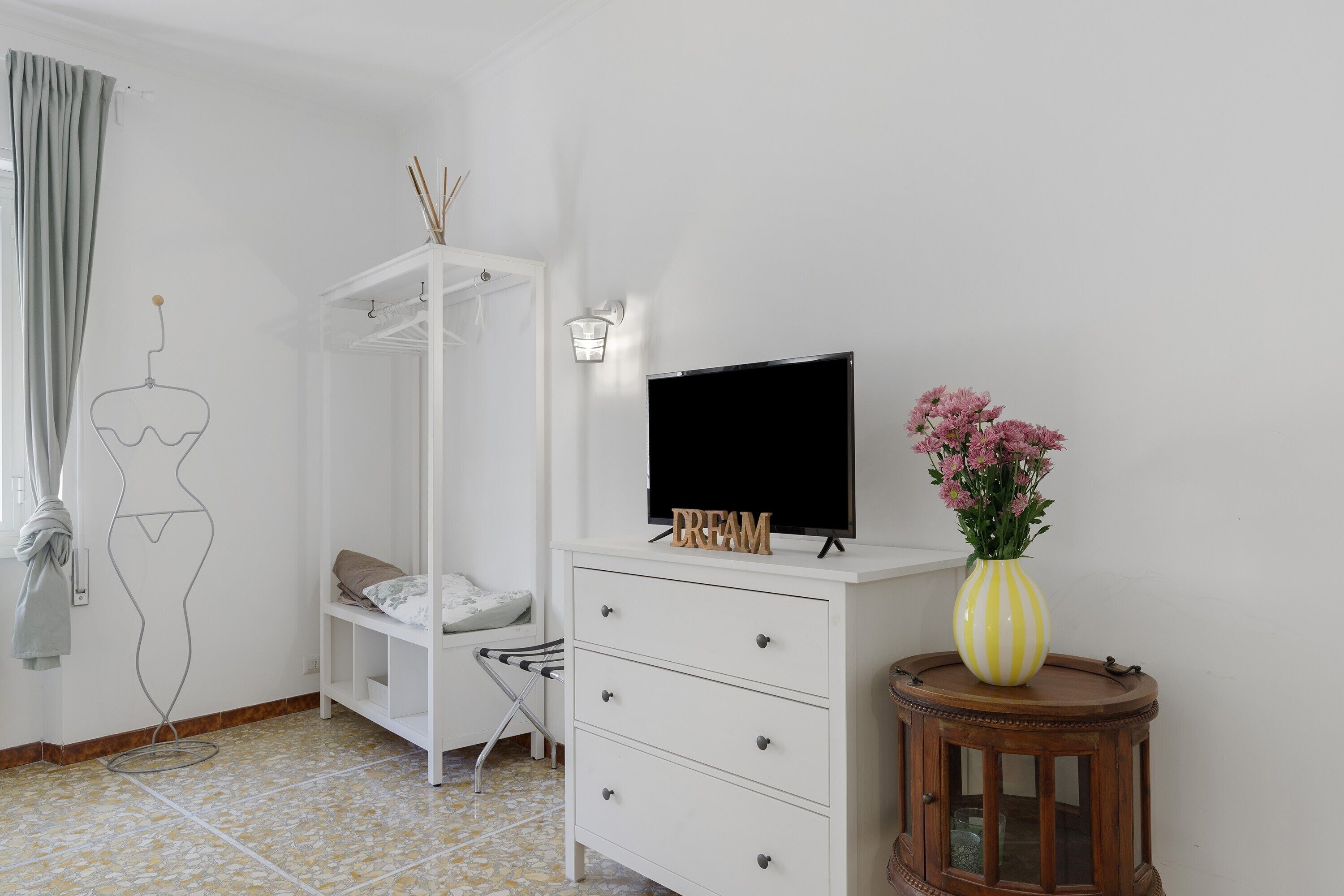 A bedroom with a bed, a TV, a dresser, a wardrobe, and a small table with a vase.