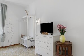 A bedroom with a bed, a TV, a dresser, a wardrobe, and a small table with a vase.