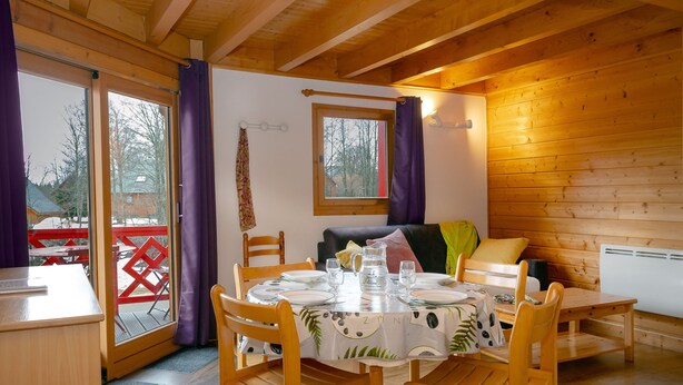 A wooden interior with a dining table set for four, a sofa, and a window with curtains.