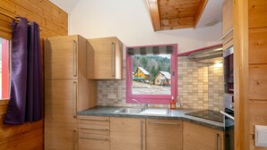 A kitchen with wooden cabinets, a sink, and a window with a view of houses.