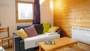 A cozy room with a sofa, a wooden table, a window with curtains, and a radiator.