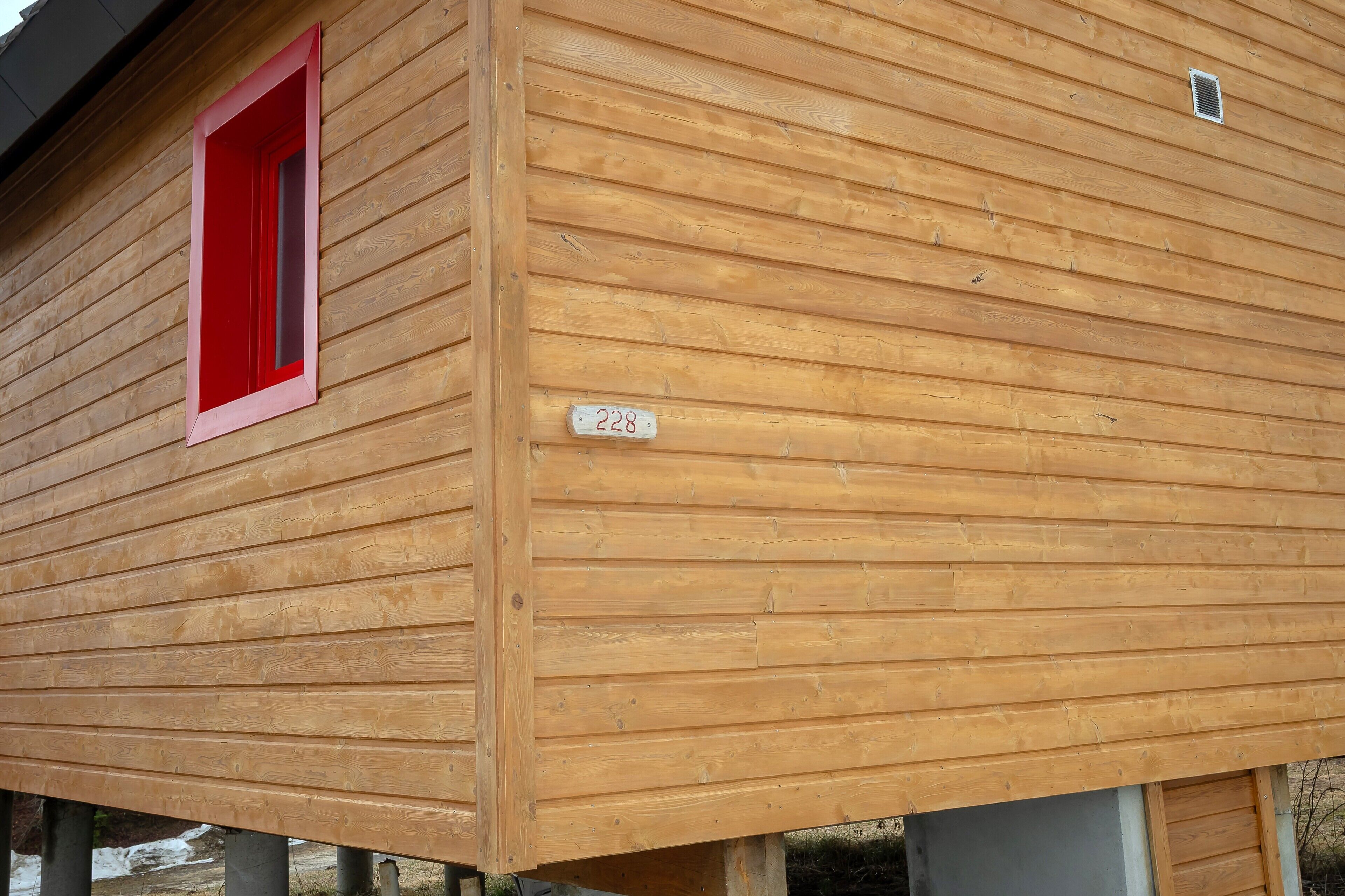 Een houten chalet met een rood raam en een nummerplaat.