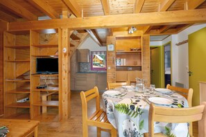 A wooden interior with a dining table set for four, wooden shelves, and a television. - Chalet '228 - Village Nordique' with Mountain View, Shared Pool and Private Terrace (Les Deserts)