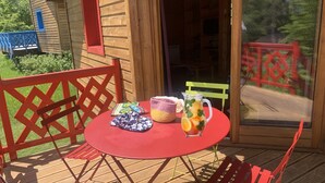 A wooden cabin with a deck, a red table with a pitcher of lemonade, and a crocheted bag.