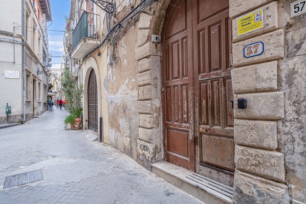 Una calle estrecha con edificios históricos, una puerta de madera grande y un letrero con el número 57.