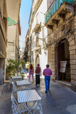A narrow street with outdoor seating, stone buildings, and a signboard.