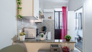 A compact kitchen with a microwave, toaster, and small refrigerator. There is a potted plant on the counter and a decorative item on the wall.