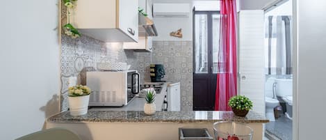 A compact kitchen with a microwave, toaster, and small refrigerator. There is a potted plant on the counter and a decorative item on the wall.