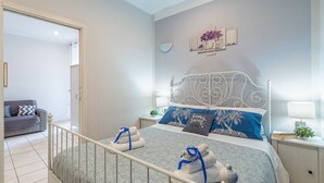 A neatly arranged bedroom with a bed, bedside tables, a nightstand, a sofa, and a door leading to another room.