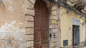 A weathered building with a large wooden door, a small window, and a sign indicating a business.