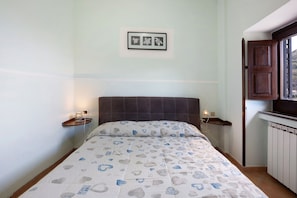Un dormitorio con una cama, mesitas de noche, un cuadro enmarcado en la pared y una ventana con vistas.