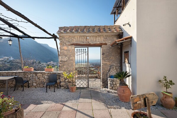 A stone patio with chairs, potted plants, and a view of the mountains.