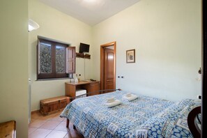 A bedroom with a bed, a desk, a chair, a television, and a window.