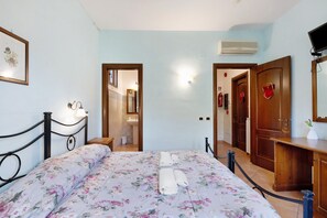 Ein Schlafzimmer mit einem Bett, einem Nachttisch, einer Holzkommode, einem Spiegel und einer Tür zu einem anderen Raum.