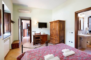 A bedroom with a bed, wooden wardrobe, television, and a bathroom with a sink and mirror.