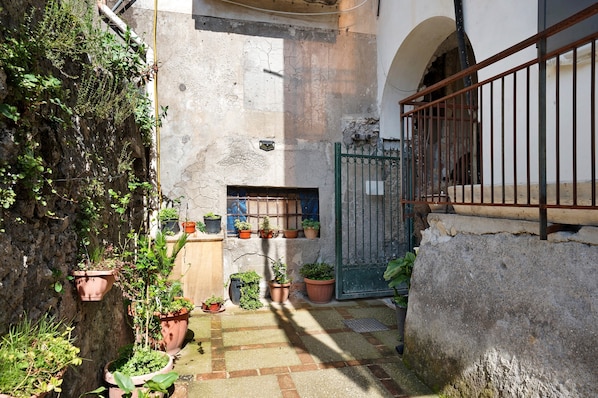 A narrow courtyard with potted plants, a metal gate, and a stone wall.