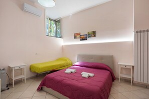 A bedroom with two beds, a radiator, a window, and artwork on the wall.