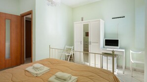 Ein Schlafzimmer mit Bett, Kleiderschrank, Schreibtisch mit Computer und Stuhl.
