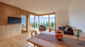 Ein modernes Wohnzimmer mit Holzboden, einem Esstisch mit Obstschale, einer Couch und einem an der Wand befestigten Fernseher.