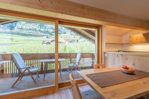 Un patio di legno con tavolo e sedie, una ciotola di frutta e vista su un vigneto.