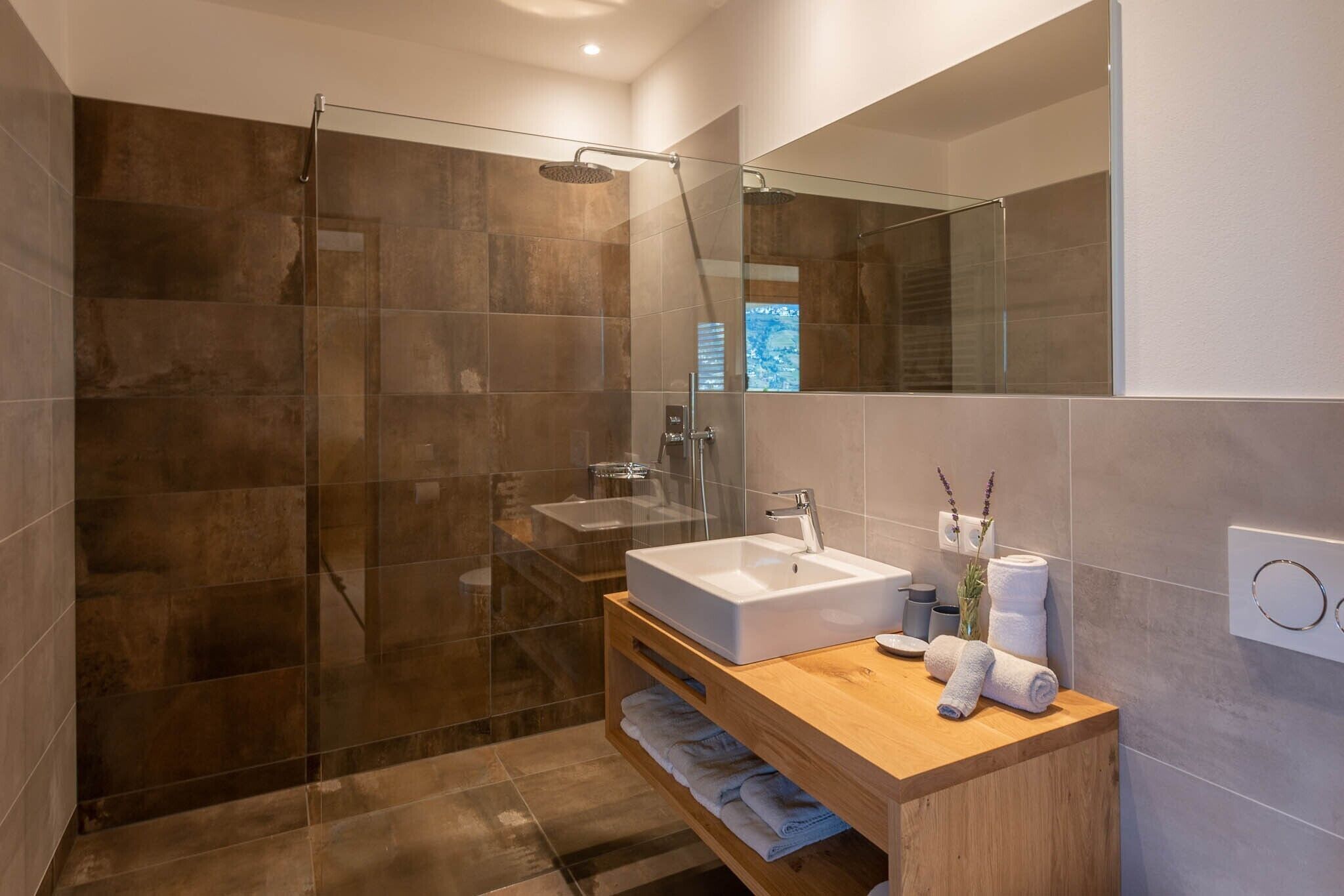Een moderne badkamer met een douchecabine van glas, een houten wastafelmeubel en een grote spiegel.