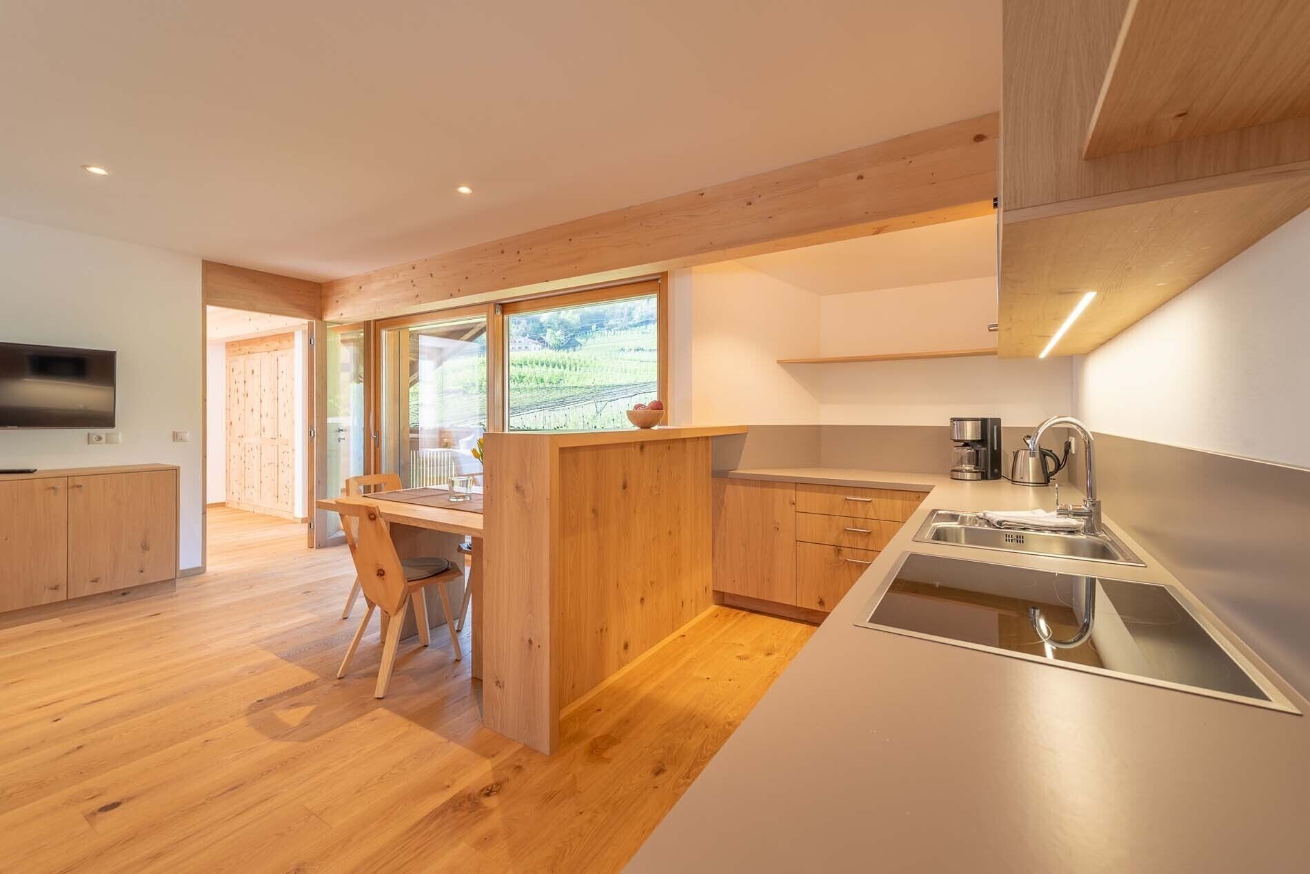 Una cocina moderna con armarios de madera, horno integrado y un amplio ventanal con vistas a un viñedo.