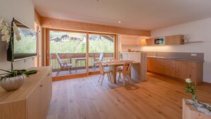 Une cuisine moderne avec des meubles en bois, un coin repas avec une table et des chaises, et une grande porte-fenêtre coulissante donnant sur une terrasse.